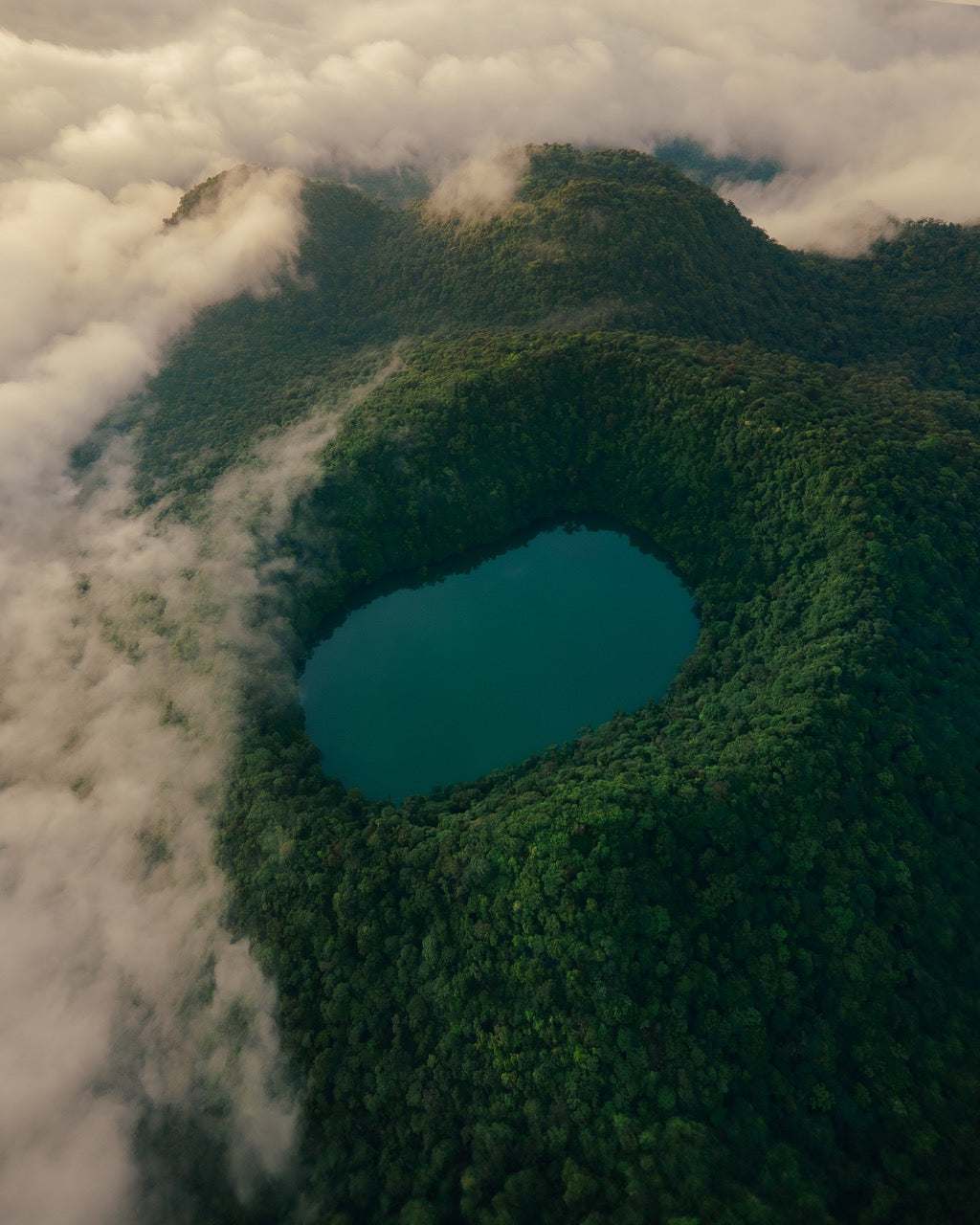 Laguna turquesa en un cráter cubierto de selva, entre nubes